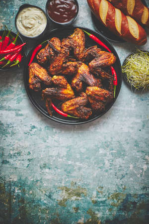 Grilled chicken wings with chilli pepper on a rustic plate served with various dips and breadの写真素材