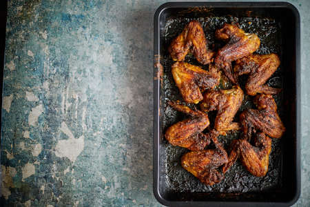 Grilled chicken wings in spices in black metal baking tray on stone table. Top viewの写真素材