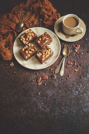 The square pieces of delicious caramel cake with peanuts and brazil nuts served with milk coffeeの写真素材