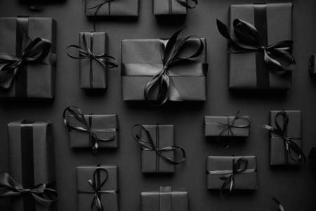 Dark Christmas theme. Square boxed gifts wrapped in black paper and ribbon arranged on blackの写真素材