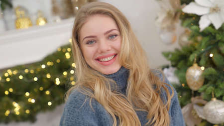 Fashionable smiling woman wearing knitwear cozy sweater in front of christmas treeの写真素材