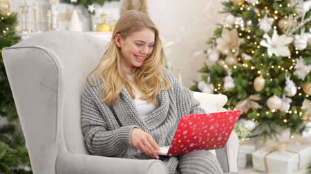 Portrait of smiling woman holding laptop on her laps and working. Sitting on comfortable armchairの写真素材
