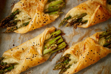 Baked green asparagus in puff pastry sprinkled with sesame seeds. Placed on a white baking paperの写真素材