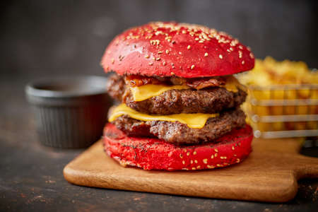 Homemade red sesame bun double bacon cheese burger. Served with french fries on wooden board.の写真素材