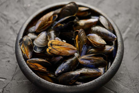 Fresh and raw sea mussels in black ceramic bowl placed on dark stone background