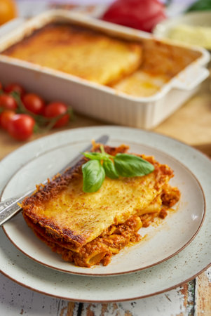 Homemade tasty meat lasagna with fresh basil and parmesan cheese in a plate on wooden backgroundの写真素材