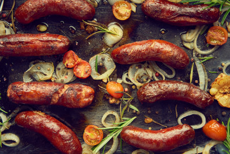 Top view on delicious grilled sausages served with onion, tomatoes, garlic, bread and herbsの写真素材