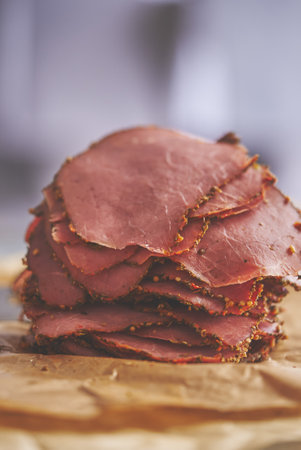 Fresh and delicious stack of sliced pastrami meat placed on wooden cutting boardの写真素材