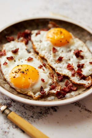 Two fresh fried eggs with crunchy crisp bacon served on rustic plateの写真素材