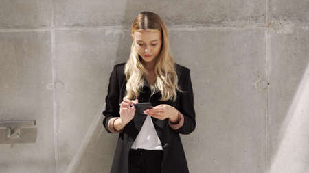 Businesswoman browsing cellphone near concrete wallの写真素材