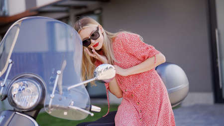 Young woman correcting makeup near scooter