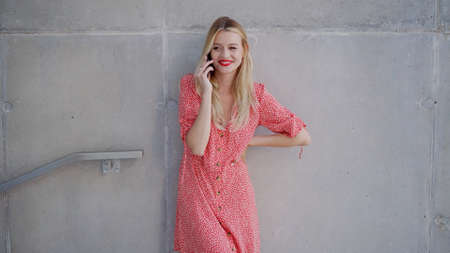 Stylish female speaking on smartphone near concrete wall