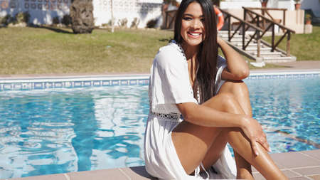 Happy woman in swim wear sitting on poolsideの写真素材