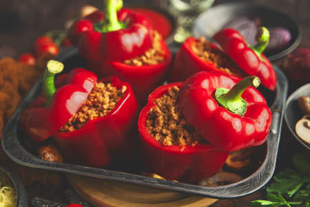 Red bell stuffed paprika peppers in iron cooking pot with various ingredients on sideの写真素材
