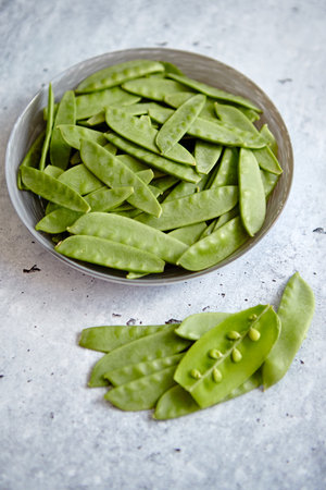 Fresh green peas in white ceramic bowl on gray stone backgroundの写真素材