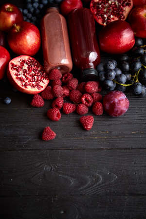 Various fresh red, purple black fruits. Mix of fruits and bottled juices on blackの写真素材