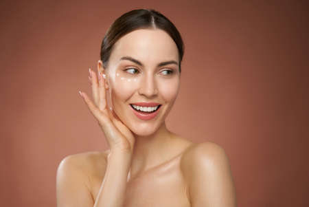 Smiling woman applying cream on faceの写真素材