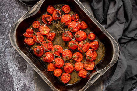 Tray of roasted red cherry tomatoes with garlic, herbs and oliveの写真素材