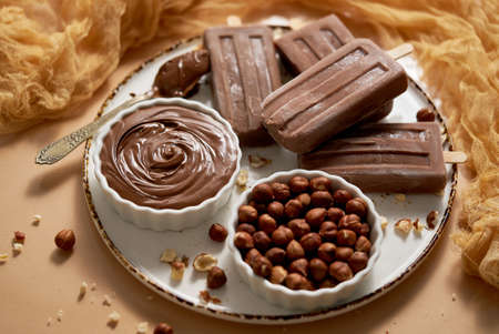Chocolate popsicles with hazelnuts served with melted chocolate on a white plateの写真素材