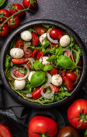 Salad with traditional italian mozzarella cheese with arugula and tomatoes on dark concrete tableの写真素材