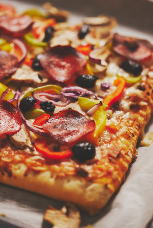 A piece of square pizza with basil pepperoni tomatoes and mushrooms on a iron trayの写真素材