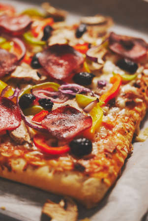 A piece of square pizza with basil pepperoni tomatoes and mushrooms on a iron trayの写真素材