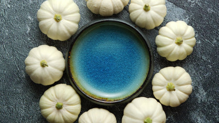 Small white Baby boo mini pumpkins placed in circle with blue ceramic bowl in the middleの写真素材