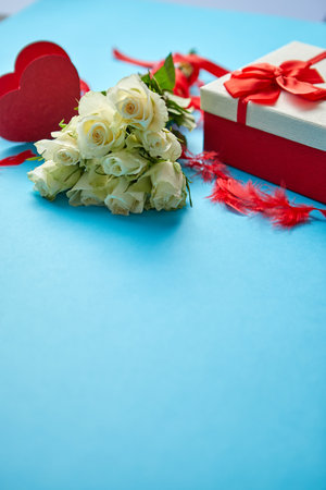 Bouquet of white roses with red bow on blue background. Boxed gift on sideの写真素材