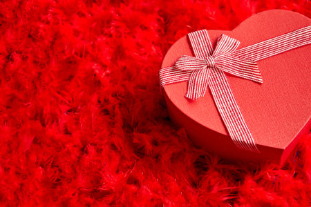 Heart shaped boxed gift, placed on red feathers backgroundの写真素材