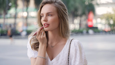 Young woman in summer dress fixes makeup outdoorsの写真素材