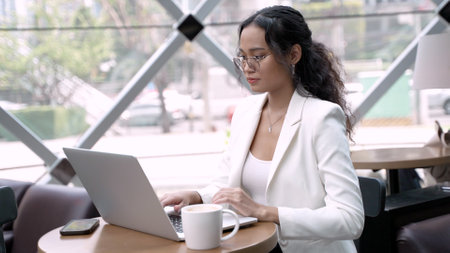 Businesswoman Using Wireless Tech and Laptop While Enjoying Coffeeの写真素材