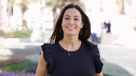 A cheerful, mature woman enjoying a leisurely walk in a sunny park in Spain, radiating positivity and confidence.の写真素材