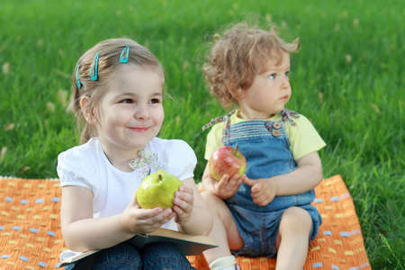 Two small lovely girls with book and fruits on the meadowの写真素材