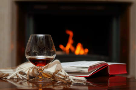 Cognac, book and shawl by the fireplaceの写真素材