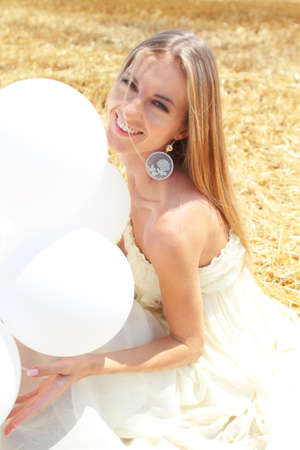 Blond smiling girl with white balloons in the fieldの写真素材
