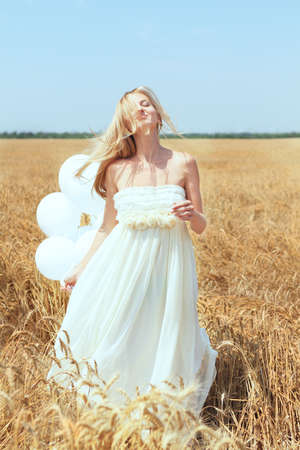 Blond smiling girl with white balloons in the fieldの写真素材