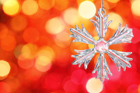 Snowflake on branch of Christmas tree against red blurred backgroundの写真素材