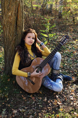Beautiful brunette guitar player girl in the autumn forestの写真素材
