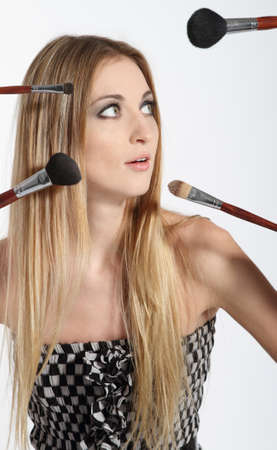 Beautiful young blonde woman with bright make-up and many brushes over her faceの写真素材