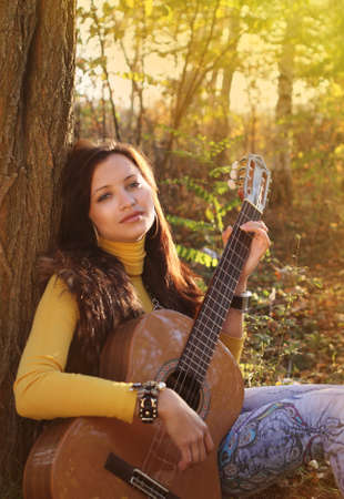 Beautiful brunette guitar player girl in the forestの写真素材