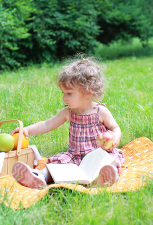 Small lovely girl with fruits and book in the parkの写真素材