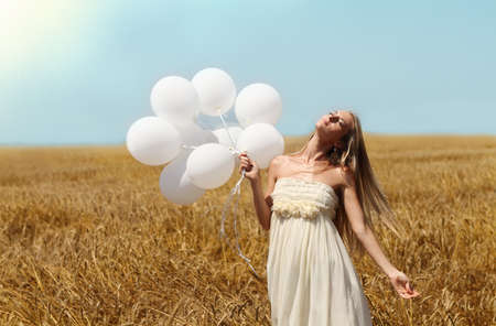 Blond smiling girl with white balloons in the fieldの写真素材