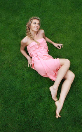Young attractive blond girl in the pink dress on the green grassの写真素材