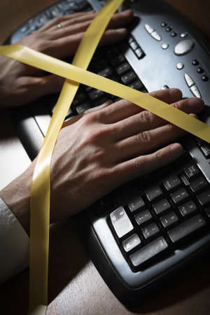 Close-up of a man's hand with duct tape typing at a computer keyboardの写真素材
