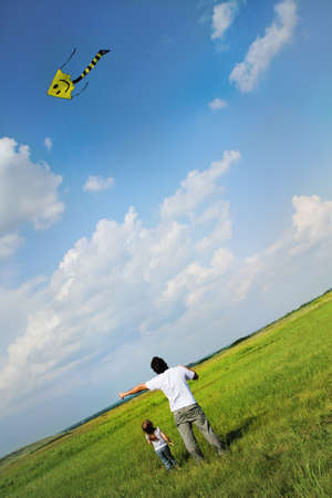 Little girl and her father with flying a kite in the summer fieldの写真素材