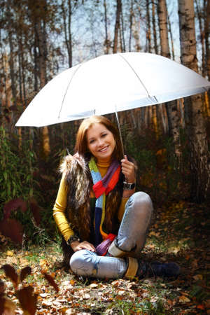 Young attractive smiling girl under umbrella in autumn forestの写真素材