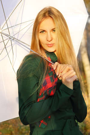 Young blond girl with white umbrella in autumn park in the eveningの写真素材