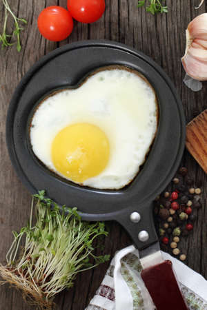 Fried egg in heart-shaped form with cress, tomato, garlic and pepperの写真素材