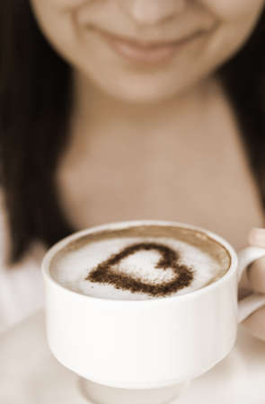 Smiling woman with cup of coffee decorated with heartの写真素材