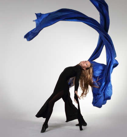 Young blond woman dancing with blue fabric over whiteの写真素材